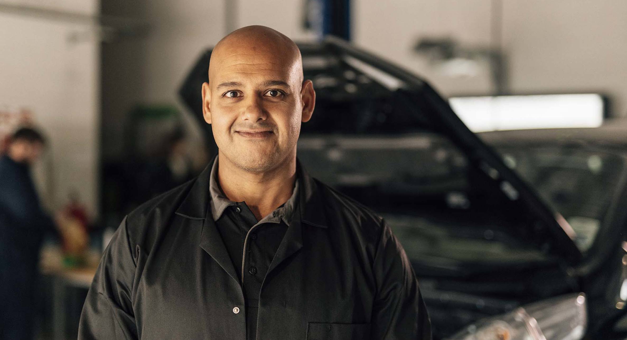 New College Lanarkshire lecturer standing in automotive workshop with electric car in background